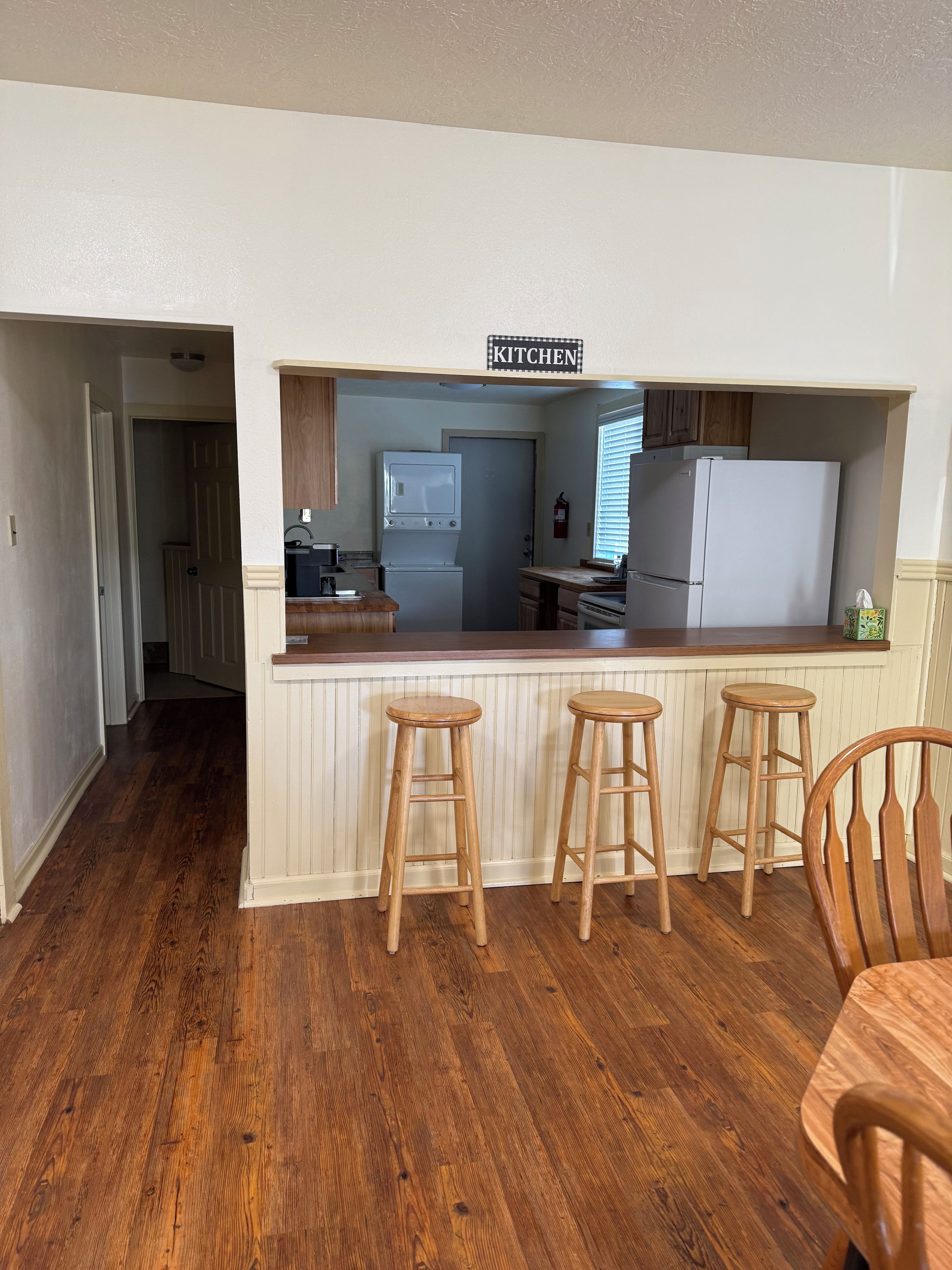 Une cuisine avec un coin bar, des tabourets en bois et un panneau indiquant l’emplacement de la cuisine.