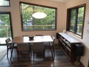 Ein Essbereich mit Holztisch und -stühlen, großen Fenstern mit Blick auf Grünflächen und einer eingebauten Bücherwand mit Fernseher.