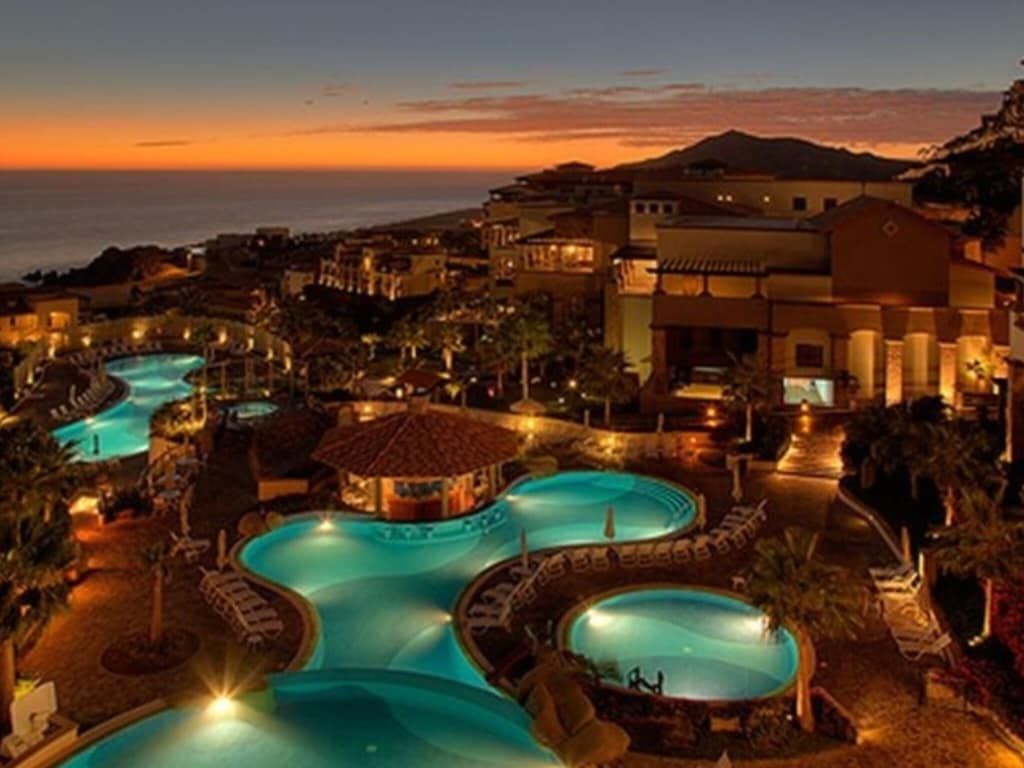 A resort with multiple swimming pools, a beach view, and a mountainous backdrop.