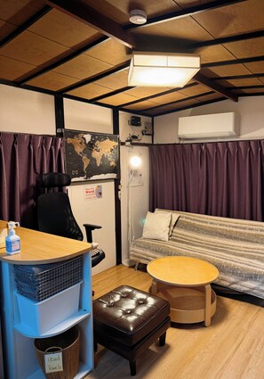 A compact living space with a sofa, a small round table, a chair, a wooden floor, and a map on the wall. - Beginning House - Authentic Japanese-Style Renovated Accommodation, Direct Access to the Airport + Disney Bus (葛飾区青戸)