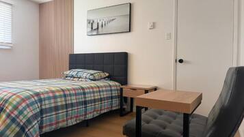 A bedroom with a bed, a chair, a desk, and a door.