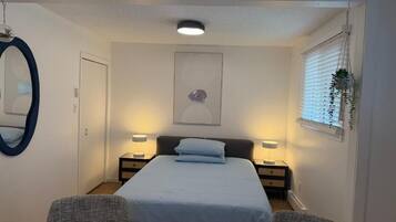 Une chambre à coucher comprenant un lit, deux tables de chevet, un miroir et une fenêtre avec des stores.