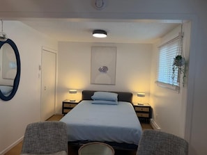 A bedroom with a bed, two bedside tables, a mirror, and a window with blinds. - Holiday Collection (Winnipeg)