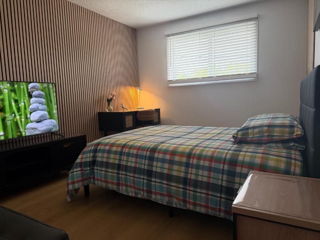 Un dormitorio con cama, mesita de noche, lámpara, televisor y ventana con persianas.