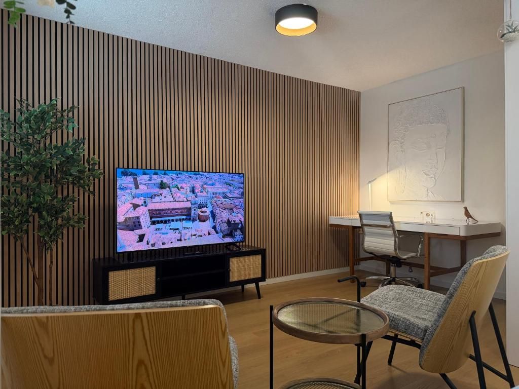 Una sala de estar moderna con televisor, una mesa de comedor, sillas y un panel decorativo en la pared.