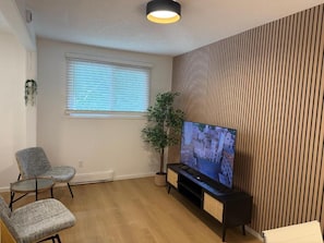 Una sala de estar con televisor de pantalla plana, dos sillones, una planta en maceta y un panel de pared de madera.