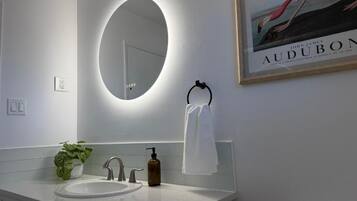Une salle de bain moderne avec un miroir rond, un lavabo, un porte-serviettes et un tableau encadré au mur.