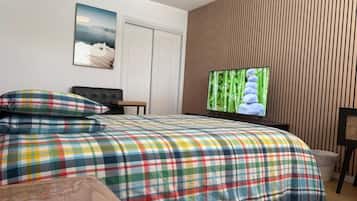 A bedroom with a plaid bedspread, a television on the wall, and a wooden panel wall.