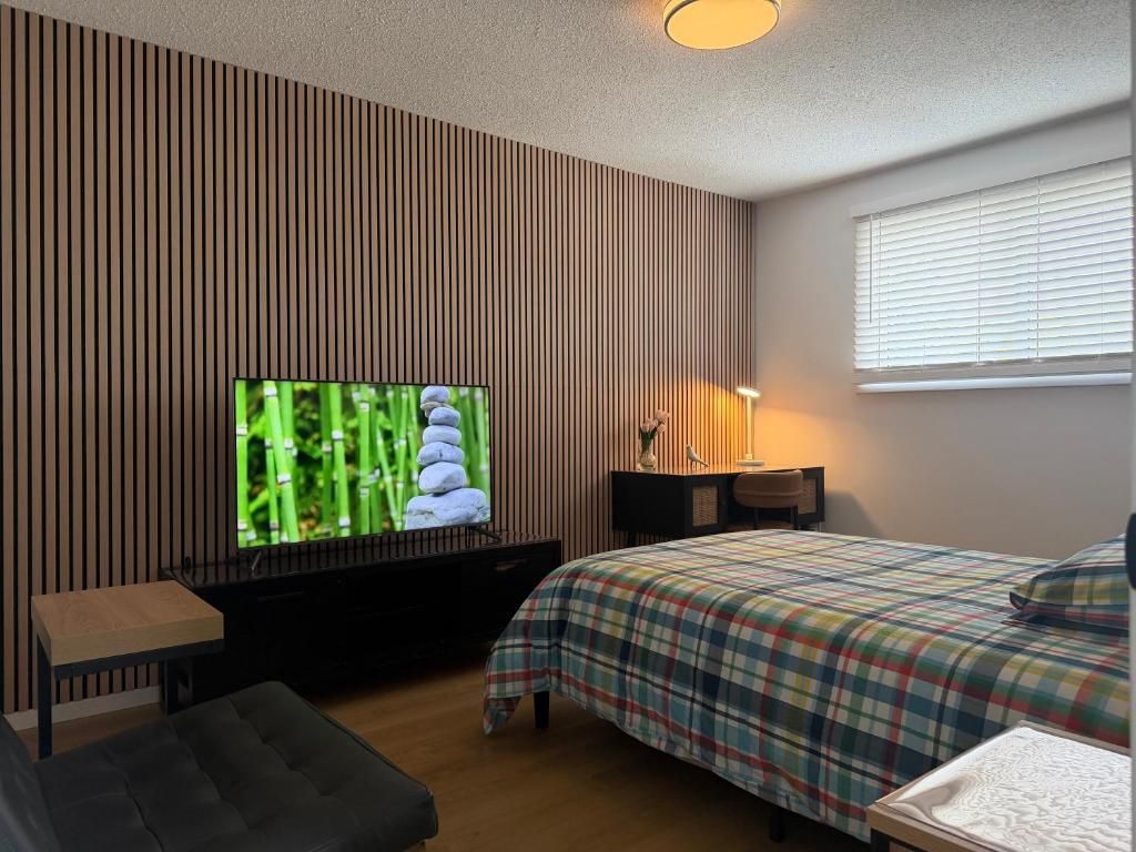 Ein Schlafzimmer mit Fernseher auf einem Schrank, einem Bett mit kariertem Überwurf, einem Nachttisch und einem Fenster mit Jalousien.