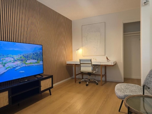 Una sala de estar moderna con un televisor de pantalla plana, una pared con listones de madera, un escritorio con una silla y una mesa de vidrio.