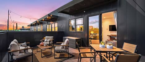 A rooftop terrace with outdoor seating and a view of the city skyline at dusk.