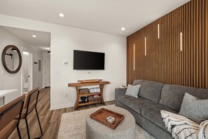 A modern living room with a grey sofa, a wooden sideboard, a flat-screen TV, and a round coffee table. - Modern Condo-5 Min to Broadway -Walk to Coffee (Nashville)