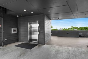 A modern elevator with a metallic finish, a black mat at the entrance, and a cityscape view through the open door. - Modern Condo-5 Min to Broadway -Walk to Coffee (Nashville)