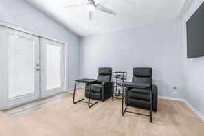 Ein Zimmer mit zwei schwarzen Ledersesseln, einem kleinen Tisch, einem Deckenventilator und einer Schiebetür aus Glas.