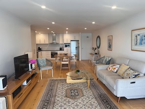 A modern living space with a sofa, TV, and a dining area with chairs and a table. - Waterfront escape with lake views, private pontoon & balcony, 5 mins to beach. (Tennyson)