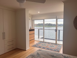 A bedroom with a large window, a wardrobe, a bed, and a view of a body of water. - Waterfront escape with lake views, private pontoon & balcony, 5 mins to beach. (Tennyson)