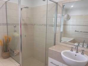 Een badkamer met een douche met glazen wand, een wastafel met twee kraan en een spiegel boven de wastafel.
