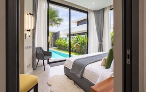 A modern bedroom with a large bed, a small desk, and a view of a swimming pool. - 3 bedrooms Villa PRIMA with pool by TVC (Tambon Choeng Thale)