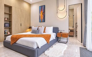 Un dormitorio moderno con una cama grande, un armario, una mesita de noche y un baño visible a través de una puerta abierta.
