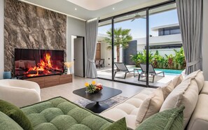 A modern living room with a fireplace, a poolside area, and a view of the outdoors. - 3 bedrooms Villa PRIMA with pool by TVC (Tambon Choeng Thale)