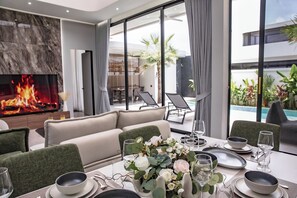 Una sala moderna con chimenea, una zona de comedor para dos personas y vistas al área de la piscina exterior.