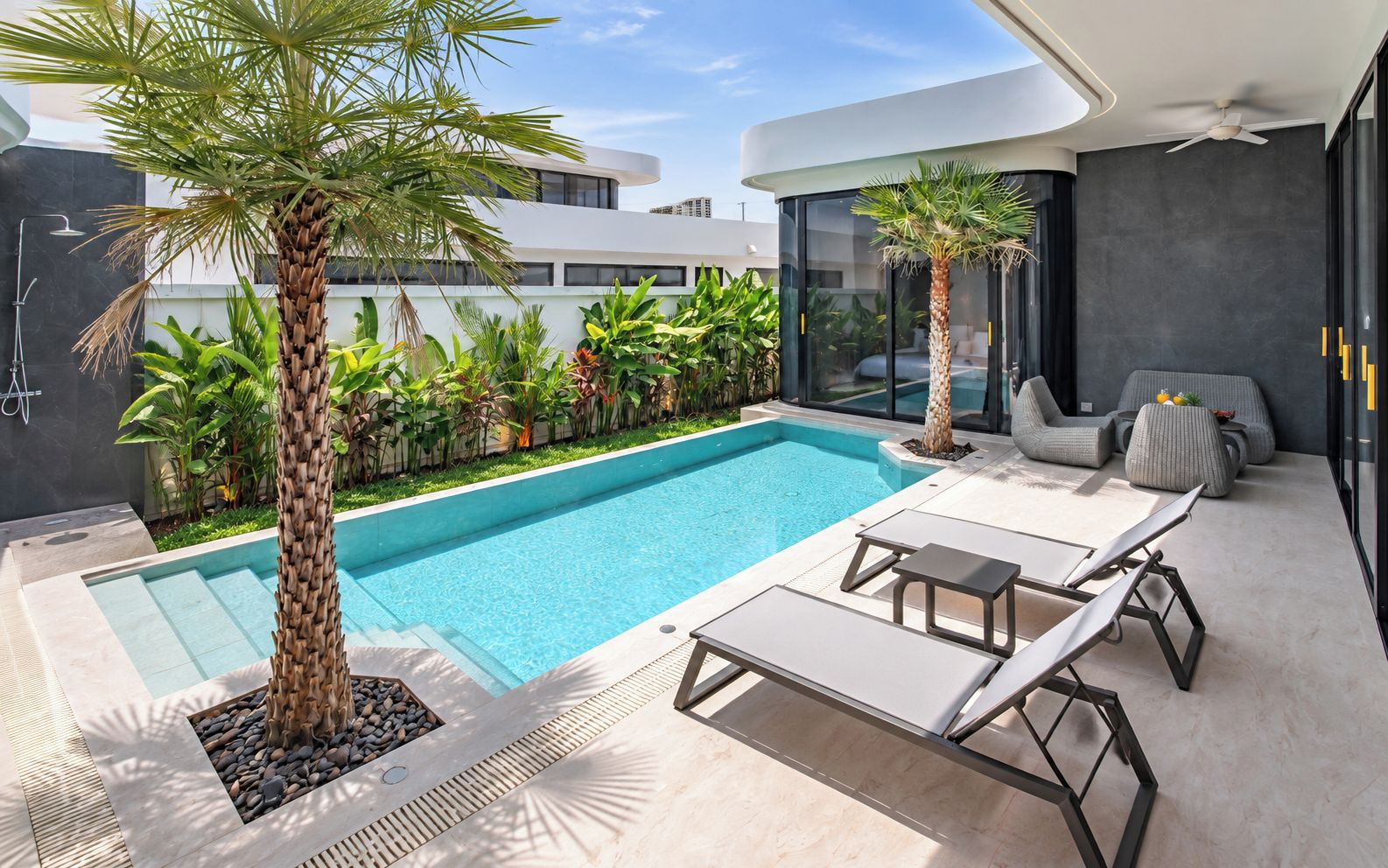Un espace piscine extérieur moderne, doté de chaises longues, d’un palmier et d’un bâtiment entièrement vitré.