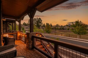 A covered outdoor area with wicker furniture and stone walls, overlooking a residential street and a mountain. - Respite in the Pines | San Francisco Peaks Views | 3BR (Flagstaff)