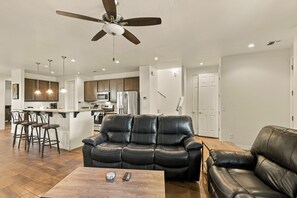 A modern living room with a leather sofa, a coffee table, and a ceiling fan. - Respite in the Pines | San Francisco Peaks Views | 3BR (Flagstaff)