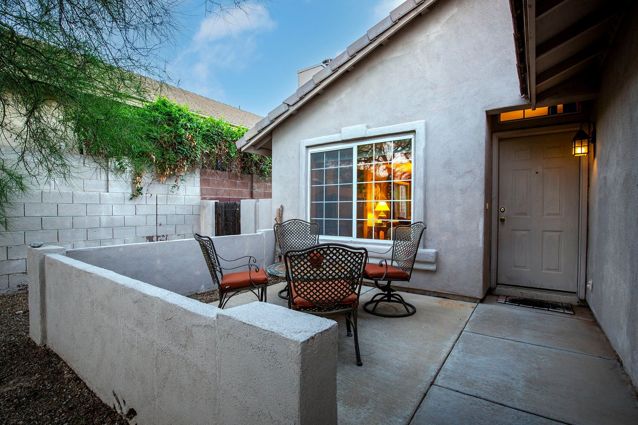 A patio with a table and chairs, a door, and a window with a lamp inside.