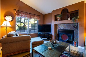 A living room with a sofa, a television, a fireplace, and a clock on the wall. - Starr Pass Vista | Golf Community | Mountain Views | 3BR (Tucson)
