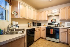 A kitchen with wooden cabinets, a sink, a dishwasher, a stove, a microwave, and a toaster. - Starr Pass Vista | Golf Community | Mountain Views | 3BR (Tucson)