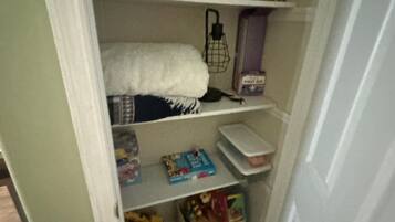 A storage closet with shelves containing various items including board games, a white towel, and storage boxes.