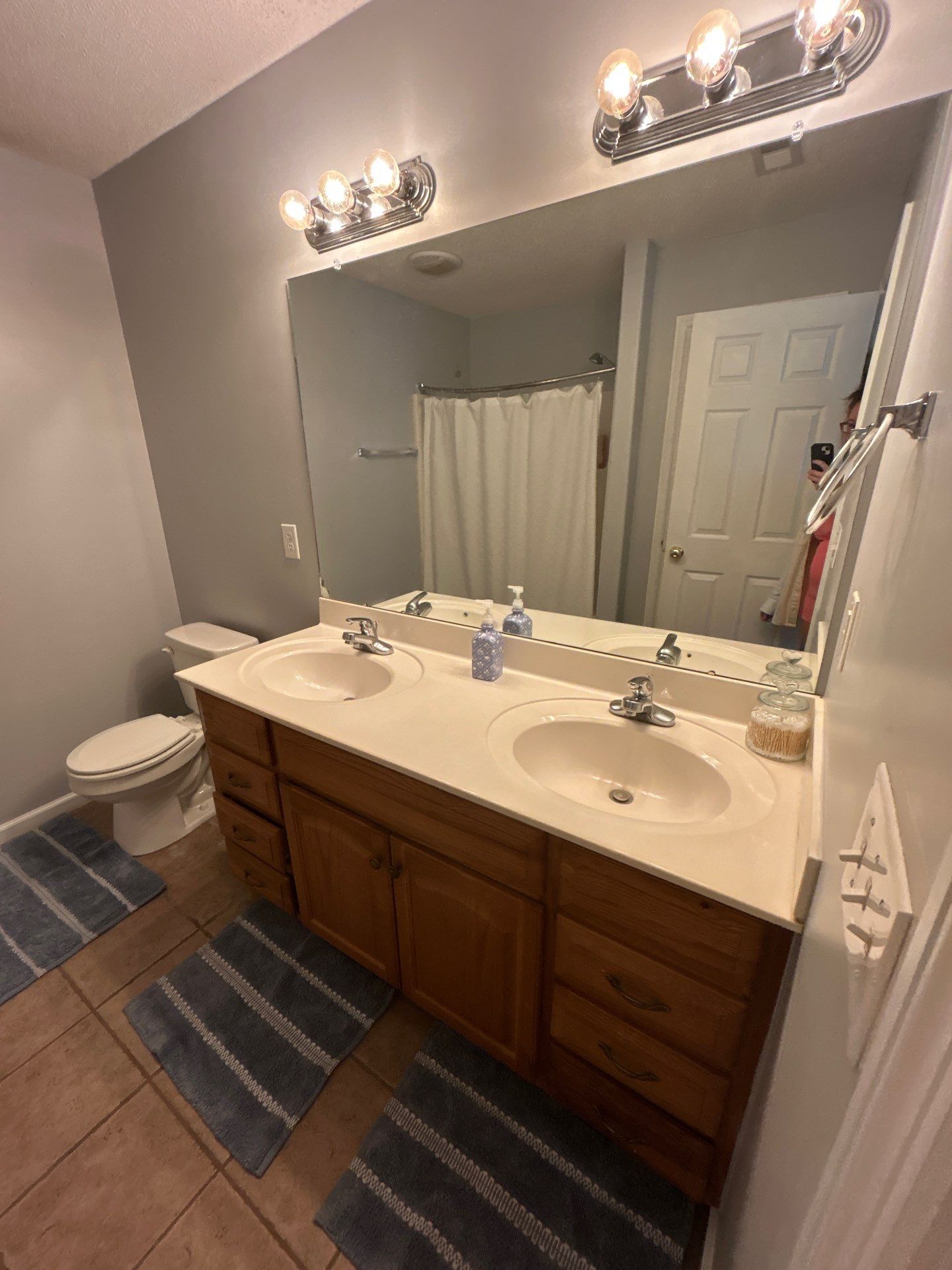 A bathroom with two sinks, a toilet, a shower curtain, and a mirror with lights.