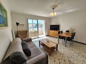 A living room with a sofa, a coffee table, a TV, a dining table with chairs, and a kitchen area with a microwave. - Appartment 1 room, A/C, all on foot (LA SEYNE SUR MER)