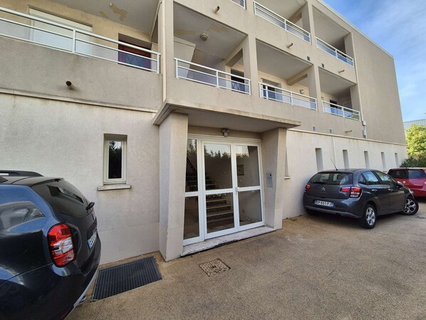 A multi-story building with a ground-level entrance, a balcony on the second floor, and a parking area with cars. - Appartment 1 room, A/C, all on foot (LA SEYNE SUR MER)