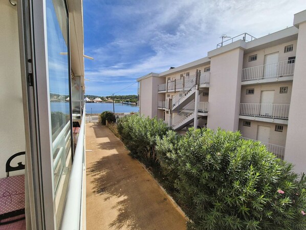 A corridor with a view of a body of water and a building with multiple balconies. - Appartment 1 room, A/C, all on foot (LA SEYNE SUR MER)