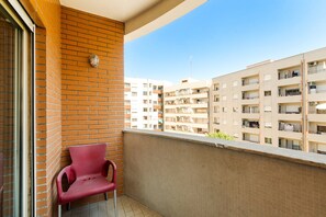 Ein Balkon mit einem roten Stuhl, einer Backsteinmauer und Blick auf mehrstöckige Gebäude.