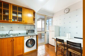 Een compacte keuken met houten kasten, een wasmachine, een magnetron en een eethoek met een tafel en stoelen.