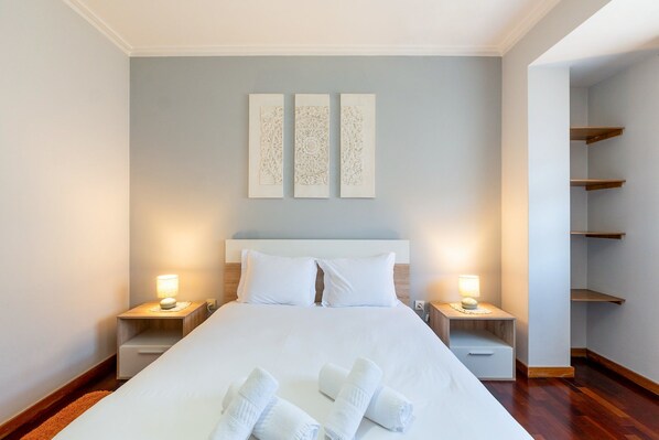 A hotel room with a large bed, two bedside tables with lamps, and three wall-mounted decorative panels.