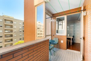 A balcony with a view of adjacent buildings, a table with chairs, and a hanging light fixture.