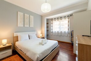 Ein Schlafzimmer mit einem Bett, Nachttischen, einem Schrank, einer Lampe und einem Fenster mit Vorhängen.