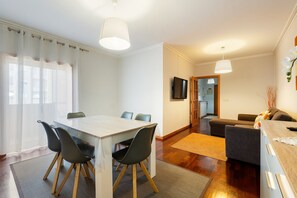 A modern living room with a dining area, wooden flooring, and a flat-screen TV mounted on the wall.