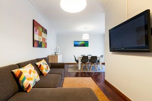A living room with a sofa, a TV, a dining table with chairs, and artwork on the walls.