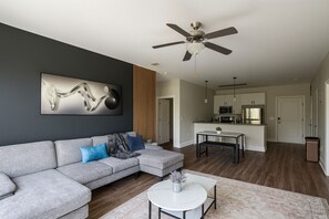 A modern living room with a grey sectional sofa, a ceiling fan, and a kitchen in the background. - Spacious 2BR/2BA Condo Across from UAB 3F (Birmingham)