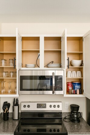 A kitchen with a built-in microwave, oven, and coffee maker. There are shelves with glassware and jars. - Spacious 2BR/2BA Condo Across from UAB 3F (Birmingham)