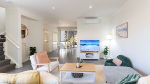 A modern living room with a television, seating, and a staircase. - Capel Sound Coastal - BBQ, Courtyard & Beach (Capel Sound)