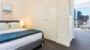 A bedroom with a bed, a nightstand, a framed picture, a wardrobe, and a view of an outdoor seating area. - Capel Sound Coastal - BBQ, Courtyard & Beach (Capel Sound)