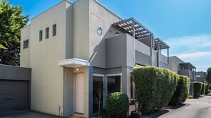 A modern two-story building with a garage, a covered outdoor area, and neatly trimmed hedges. - Capel Sound Coastal - BBQ, Courtyard & Beach (Capel Sound)