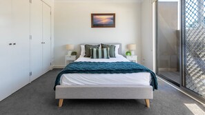 A bedroom with a bed, a nightstand with a lamp, a framed picture on the wall, and a sliding glass door leading to a balcony. - Capel Sound Coastal - BBQ, Courtyard & Beach (Capel Sound)