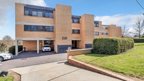 A multi-story residential building with a parking garage, a well-maintained lawn, and a hedge. - Garran Treetop Views - Balcony & Mountain Sunsets (Garran)